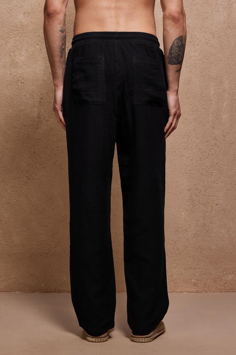May include: Black linen pants with a relaxed fit, featuring two back pockets and a drawstring waist. The pants have a wide leg design and are made of a lightweight fabric, suitable for casual wear. The pants are shown from the back.