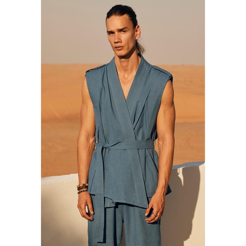 May include: A teal-coloured sleeveless wrap top and matching trousers. The top has a V-neck and a waist tie. The outfit is made of a lightweight fabric. The model is wearing a bracelet. The outfit is suitable for warm weather.