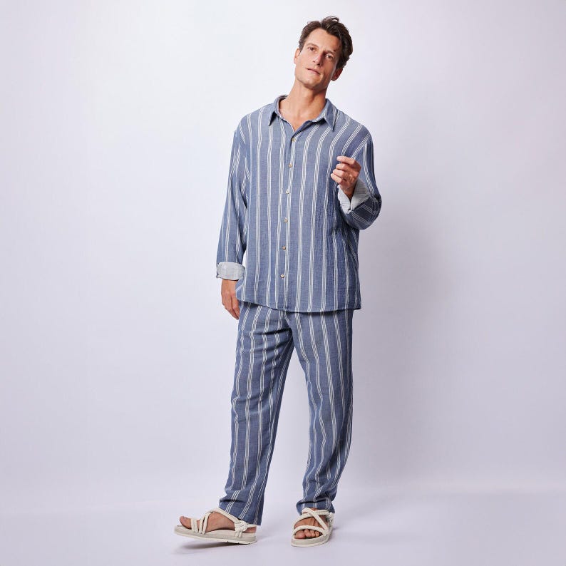 May include: A blue and white striped pajama set, consisting of a button-down shirt and matching pants. The long-sleeved shirt has a collar and cuffs, and the pants have a relaxed fit. The person is wearing white sandals.