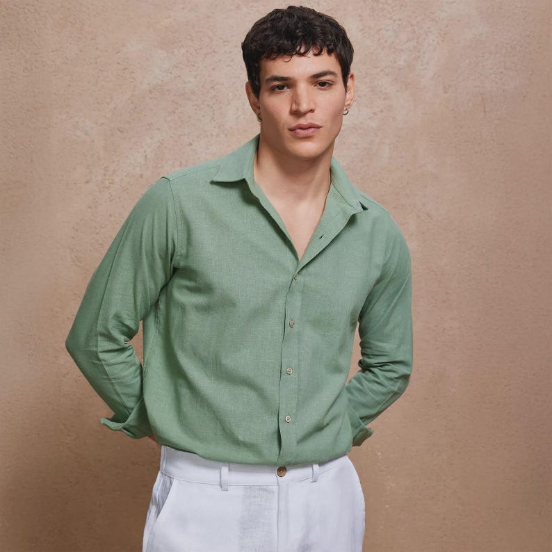 May include: A light green button-down shirt with long sleeves and a classic collar. The shirt is paired with white pants. The model is standing in front of a neutral background.