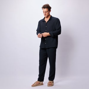 May include: A dark navy blue linen shirt and matching pants set. The long-sleeved shirt has a button-down front and the pants are straight-legged. The model is wearing beige sandals. The outfit is suitable for casual wear.