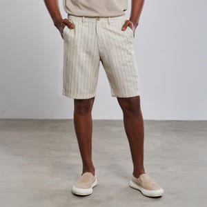May include: A pair of beige linen shorts with thin vertical white stripes. The shorts have a button and zipper closure and two front pockets.