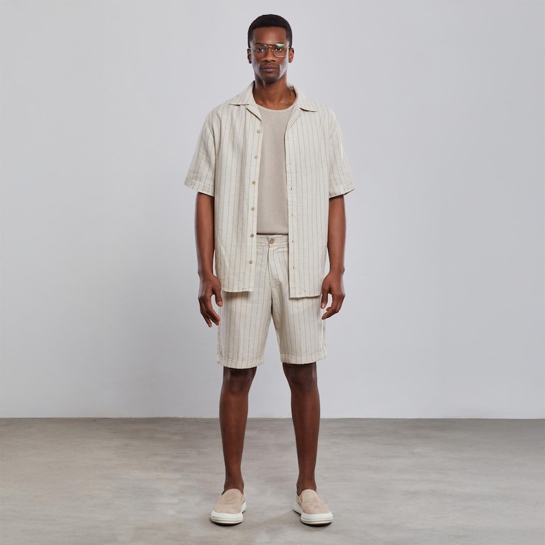 May include: A person wearing a beige striped short-sleeved shirt and matching shorts. The shirt has a collar and a button-up front. The person is wearing glasses and has short black hair.