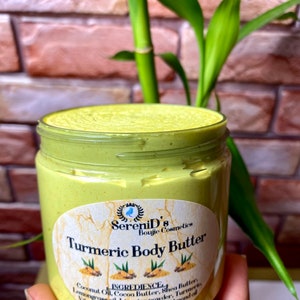 Op de afbeelding: Een pot met kurkuma body butter met een geel en groen etiket. Het etiket vermeldt "SereniD's Boujie Cosmetics Turmeric Body Butter" en somt de ingrediënten op: kokosolie, cacaoboter, sheaboter, citroengras olie, zoethoutpoeder, kurkuma, vitamine E olie, druivenpitolie, amandel olie. De pot is 200g.