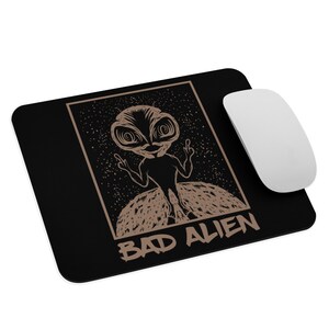 May include: A black mouse pad with a brown alien graphic and the text "BAD ALIEN". The alien is giving the middle finger with both hands.