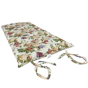 May include: A rectangular cushion with a floral pattern in shades of red, pink, blue, and green on a cream background. The cushion has ties on the sides. The cushion is designed for outdoor or indoor seating.