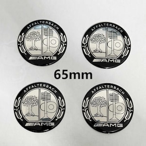 Puede incluir: Cuatro emblemas de coche redondos negros y plateados con el texto "Affalterbach" y "AMG" en blanco. Los emblemas tienen un diámetro de 65 mm.