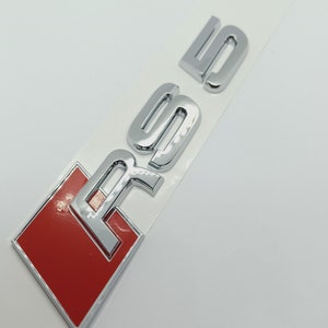 K&ouml;nnte beinhalten: Ein silbernes und rotes Autoemblem mit den Buchstaben "RS5" in erhabener Schrift.