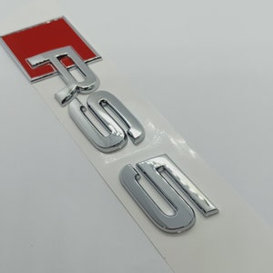 K&ouml;nnte beinhalten: Ein silbernes Chrom-Autoemblem mit den Buchstaben "RS5" in einer fetten, stilisierten Schrift. Das "R" ist rot.