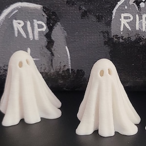 May include: Three white ghost figurines of varying sizes, with the largest ghost in the center and the smallest ghost on the left. The ghosts are standing on a black and white background with the words "RIP" written on some of the background elements.