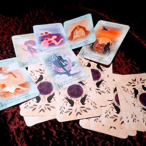 May include: A set of tarot cards with illustrations of mystical figures and symbols. The cards are on a dark red velvet surface. The cards feature titles such as "Hidden Familiars", "The Air Path", and "Antral Travels".