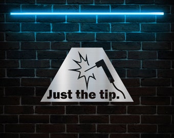 May include: A white triangular sign with a welding torch graphic and the text "Just the tip." The sign is against a dark brick wall with a blue neon light above it.