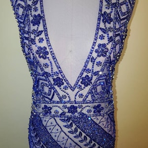 May include: A sleeveless royal blue dress with a deep V-neckline and intricate beading throughout. The beading features a geometric pattern with floral accents.