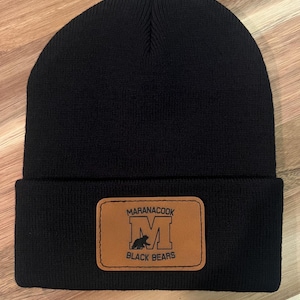 May include: Black knit beanie with a brown leather patch that says "Maranacook Black Bears" and has a black silhouette of a bear inside a white "M".