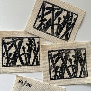 May include: Three black and white linocut prints on fabric, each depicting a stylized image of a group of swords or knives.