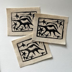 May include: Three black and white fabric patches with a stylized image of a creature with stars printed on them.