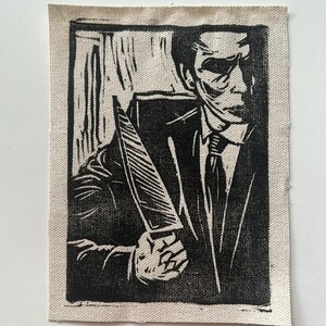 May include: A black and white linocut print on canvas depicts a figure in a suit holding a large knife. The artwork has a vintage, slightly distressed aesthetic. The figure's face is partially obscured, adding a mysterious element to the design.
