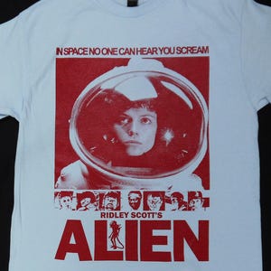 Könnte beinhalten: Hellblaues T-Shirt mit roter Grafik aus dem Film "Alien". Die Grafik enthält den Text "IN SPACE NO ONE CAN HEAR YOU SCREAM", ein Porträt einer Person in einem Weltraumhelm und den Filmtitel.