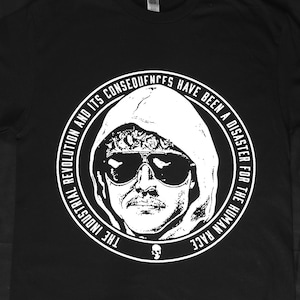 以下が含まれることがあります： サングラスとフードを着用した人物の白いグラフィックが特徴の黒いTシャツ。「THE INDUSTRIAL REVOLUTION AND ITS CONSEQUENCES HAVE BEEN A DISASTER FOR THE HUMAN RACE」というテキストがグラフィックを囲んでいます。