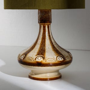 Puede incluir: Lámpara de mesa de cerámica con base texturizada marrón y crema, con rayas marrones verticales y patrones circulares decorativos. La lámpara tiene una pantalla verde.