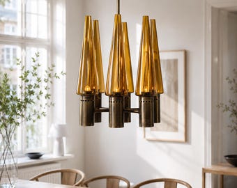 May include: A multi-light chandelier featuring a central brass fixture with a dark, weathered finish. It holds six tall, conical amber glass shades that taper toward the top. Each glass shade is positioned over a small light bulb.