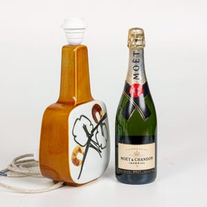 May include: A ceramic table lamp with a brown and white floral design. The lamp is next to a bottle of Mo&euml;t & Chandon Imperial Brut champagne.