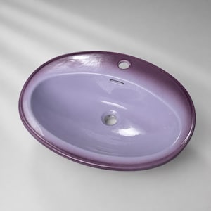 Könnte beinhalten: Ein ovales Waschbecken mit einem glatten, helllavendelfarbenen Becken, das in einen dunkleren violetten Rand übergeht. Das Waschbecken verfügt über ein zentrales Abflussloch, eine Überlauföffnung und ein einzelnes Hahnloch am oberen Rand.