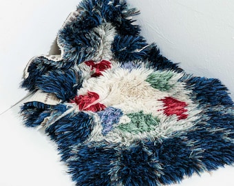 Puede incluir: Una alfombra de pelo azul, blanco, rojo y verde con un patrón geométrico. La alfombra está doblada y sobre una superficie blanca.