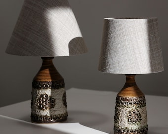 Peut inclure: Deux lampes de table avec des bases en céramique texturées brunes et blanches présentant un motif circulaire répétitif. Chaque lampe est surmontée d'un abat-jour conique en tissu gris clair avec une texture tissée et un aspect neutre.