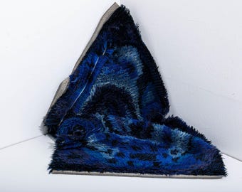Puede incluir: Una manta de piel sintética azul y negra con un ribete gris. La manta está doblada en una esquina, mostrando su suave textura y variaciones de color. La manta está hecha de un material suave y cómodo.