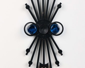Peut inclure: Applique murale en métal noir avec un motif en étoile et deux accents en verre bleu. L'applique a un porte-bougie au centre.