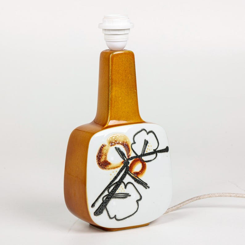 May include: A brown ceramic table lamp with a white base featuring a stylized floral design in black and brown. The lamp has a white ceramic shade.