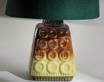 Peut inclure: Lampe de table en céramique avec abat-jour vert foncé. Le pied de la lampe est un mélange de marron, d'orange et de jaune avec un motif géométrique texturé. La lampe est de style vintage ou rétro.
