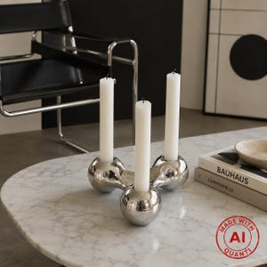 Può includere: Un candelabro in metallo color argento lucido con una forma organica arrotondata a tre punte. Contiene tre candele affusolate bianche, alte e sottili. La base è liscia e riflettente, dotata di tre supporti circolari per le candele.