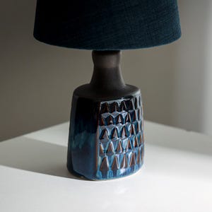 Puede incluir: Una lámpara de mesa de cerámica azul y marrón con una pantalla de tela azul oscuro. La base de la lámpara tiene un patrón geométrico.