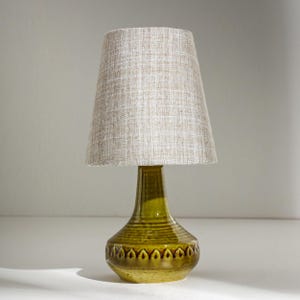 Puede incluir: Lámpara de mesa de cerámica verde oliva con base estampada y pantalla de tela beige. La lámpara tiene un diseño clásico. La pantalla mide unos 25 cm de diámetro. Un objeto decorativo para el hogar.