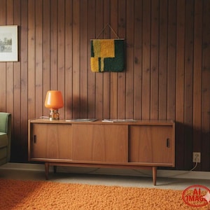 May include: A mid-century modern living room with a wooden cabinet, orange lamp, and a shag rug. The wall is paneled with vertical wooden planks. A green armchair and a framed picture are also visible.