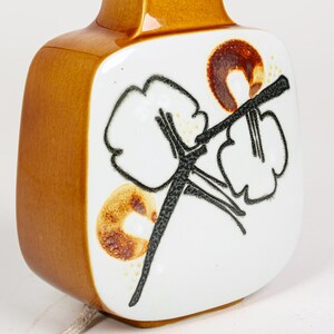 May include: A brown ceramic table lamp with a white square shade featuring a black and brown floral design.