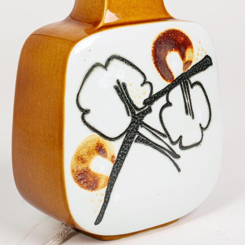 May include: A brown ceramic table lamp with a white square shade featuring a black and brown floral design.