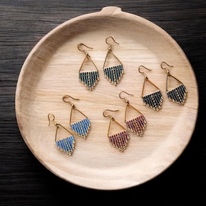 May include: Six pairs of handmade earrings with gold-coloured frames and beaded fringe in various colours, including blue, green, black, and burgundy. The earrings are displayed on a wooden tray.