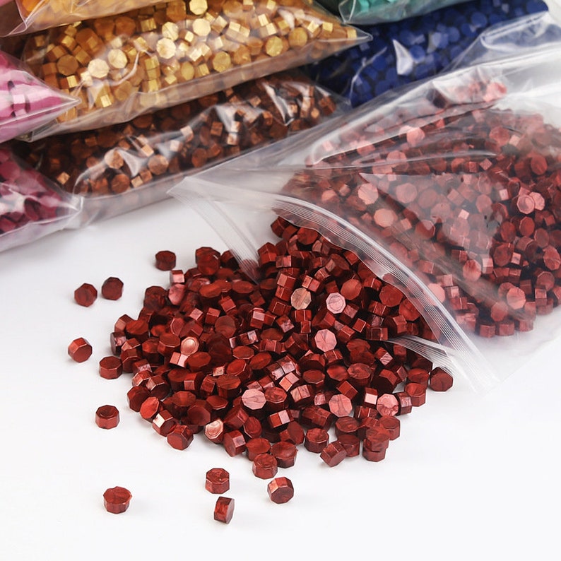 May include: A close-up of a bag of red sealing wax beads. The beads are small and round, and they are ideal for sealing envelopes or other documents.