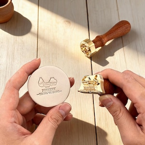 May include: A set of pottery stamps with wooden handles and brass stamp heads. One stamp is round with the text "POTTERY -THONG YU HONG-" and pottery illustrations. The other stamp has a rectangular head with a pottery design.