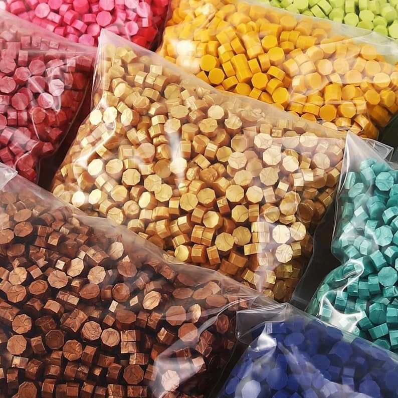 May include: Assortment of colourful wax seal stamps in clear plastic bags. The wax seals are in various colours, including red, gold, copper, green, and blue.