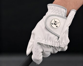May include: White golf glove with a gray trim and a circular emblem featuring golf clubs and a ball. The glove is held by a person and is designed for a right-handed golfer. The glove has small perforations for breathability.