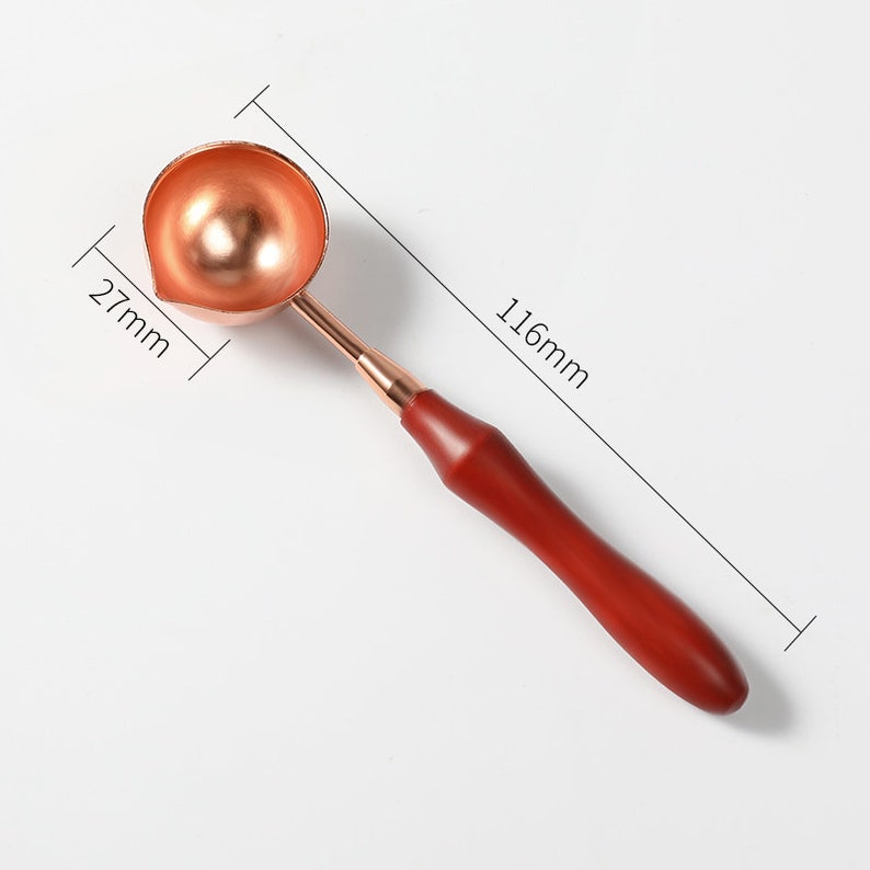 May include: A copper-coloured wax seal spoon with a wooden handle. The spoon is 2.7 inches wide and 4.6 inches long.