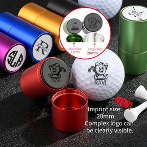 Könnte beinhalten: Eine Sammlung bunter zylindrischer Golfballstempel aus Metall in Rot, Blau, Lila, Gold und Grün sowie ein weißer Golfball mit einer Zeichentrickfigur und dem Namen RAVI. Enthält Text mit Angaben zu Abdruckgrößen von 12mm und 20mm.