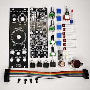 Puede incluir: Un conjunto de componentes electr&oacute;nicos para un proyecto de bricolaje, que incluye placas de circuito impreso negras, potenci&oacute;metros, interruptores y un cable de cinta multicolor. Los componentes est&aacute;n dispuestos sobre una superficie blanca, listos para el montaje.