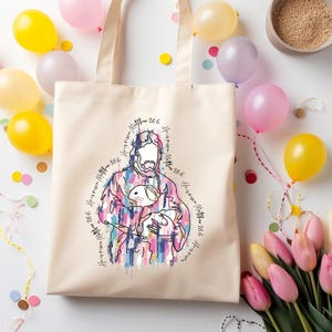 May include: A beige tote bag with a colorful graphic of a figure holding a lamb, with the text "He is risen Matthew 28:6" in a circular pattern. The bag is surrounded by balloons, confetti, and flowers.