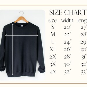 May include: A black sweatshirt hanging on a wooden hanger, with a size chart to the right. The size chart lists sizes S to 4X, with corresponding width and length measurements in inches. The sweatshirt is plain and has long sleeves.