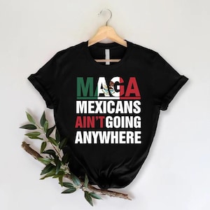 May include: Black t-shirt with the text "Maga Mexicans Ain't Going Anywhere" in white letters. The text is overlaid with a graphic of the Mexican flag.